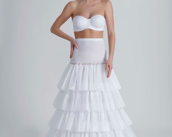 May include: A white strapless bra and a tiered petticoat. The petticoat has multiple layers of ruffled fabric, creating a full, voluminous shape. The bra and petticoat are both made of a soft, white fabric. The overall look is elegant and classic.