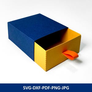 Può includere: Una scatola rettangolare con coperchio blu navy e cassetto giallo. Il cassetto ha una linguetta arancione. La scatola è parzialmente aperta, rivelando l'interno. Il testo "SVG-DXF-PDF-PNG-JPG" è nella parte inferiore dell'immagine.
