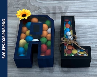 May include: Two blue and black cardboard letters, A and L, filled with colorful candy. The letters are decorated with a sunflower.
