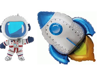 May include: Two foil balloons, one shaped like an astronaut and the other shaped like a rocket. The astronaut is wearing a white spacesuit with a blue helmet and red accents. The rocket is blue and silver with a gold flame.