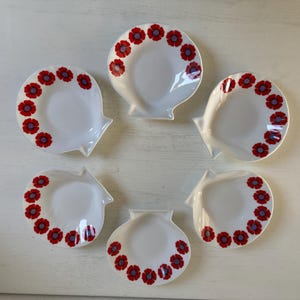 Könnte beinhalten: Sechs weiße, muschelförmige Schalen mit einem roten und lila Blumenmuster am Rand. Die Schalen sind kreisförmig auf einer weißen Oberfläche angeordnet und zeigen einen Vintage-Look.