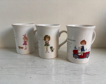 Op de afbeelding: Drie witte keramische mokken met illustraties. Eén mok toont een meisje met een kat, een andere een meisje met een hond en de derde een jongen die een rood voertuig bestuurt. Elke mok heeft een gebogen handvat.