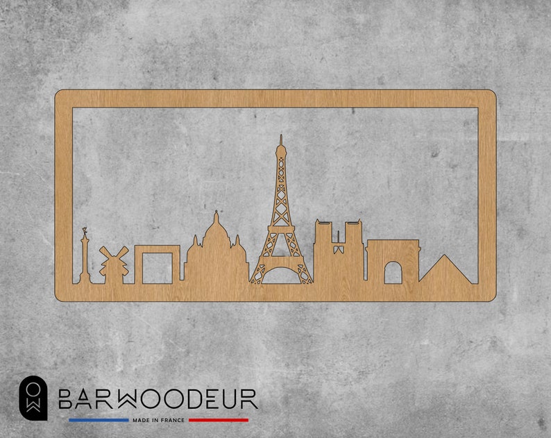 Op de afbeelding: Een houten uitsnijding van de skyline van Parijs, met iconische bezienswaardigheden zoals de Eiffeltoren, de Arc de Triomphe en de Notre Dame kathedraal. De uitsnijding is gemonteerd op een lichtbruin houten frame.