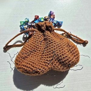 May include: A brown crocheted dice bag with a drawstring closure, filled with colorful, iridescent dice.