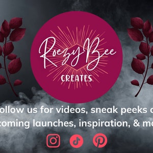 May include: A pink circle with the text "Rouzy Bee Creates" in white cursive lettering. The circle is surrounded by a burst of peach-colored rays. The background is a dark gray with a smoky effect and two dark red leafy branches on either side.