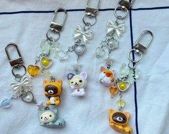 Puede incluir: Llaveros con colgantes de animales de dibujos animados. Cada llavero tiene un cierre plateado, lazos transparentes y colgantes colgantes. Los colgantes de animales son en tonos de amarillo, naranja, blanco y gris. Decorado con corazones, estrellas y perlas.