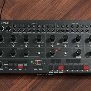 May include: A black synthesizer with numerous knobs, buttons, and ports. The word "Crave" is at the top left, and the brand name "behringer" is at the bottom right. The device has a variety of controls for sound manipulation.