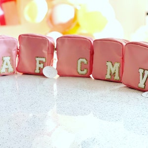 May include: Five pink zippered pouches with gold letters on the front. The letters spell out "AFCMV".