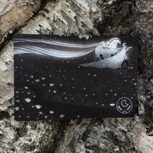 Puede incluir: Una tarjeta negra con una ilustraci&oacute;n blanca de una persona montando un caballo con una capa blanca que fluye. El fondo es azul oscuro con estrellas blancas y flores blancas. La tarjeta tiene un s&iacute;mbolo de luna creciente en la esquina inferior derecha.