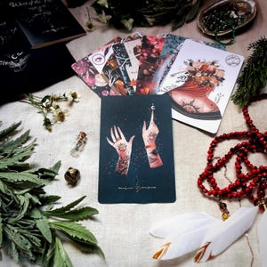Puede incluir: Una carta de tarot con un fondo azul oscuro y dos manos que se estiran hacia una luna creciente. Las manos est&aacute;n adornadas con intrincados tatuajes, incluyendo un sol y una luna creciente. La carta es parte de una baraja de tarot con un tema m&iacute;stico.