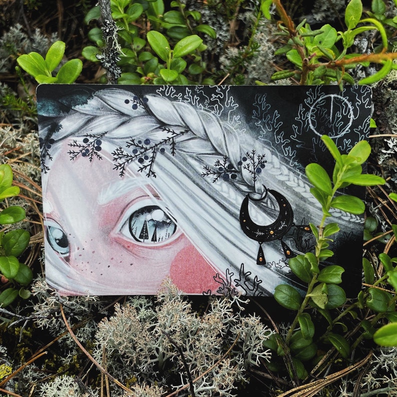 Puede incluir: Una ilustraci&oacute;n en blanco y negro de la cara de una mujer con el pelo largo y suelto. La mujer tiene una escena de bosque reflejada en su ojo. Lleva un pendiente de media luna con cuentas colgantes.