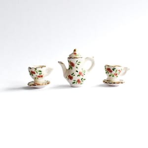Peut inclure: Un service à thé miniature en céramique composé d'une théière avec couvercle et de deux tasses sur soucoupes. Chaque pièce est blanche avec un motif peint à la main de petites fleurs rouges, de feuilles vertes et de bords dorés.
