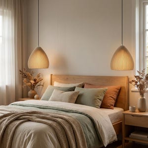 Könnte beinhalten: Zwei beige Pendelleuchten mit vertikaler Rippenstruktur hängen an dünnen schwarzen Kabeln über einem Holzbettrahmen. Das Bett ist mit geschichteter Bettwäsche in Salbeigrün und Creme bezogen und mit einer strukturierten beigen Decke bedeckt.