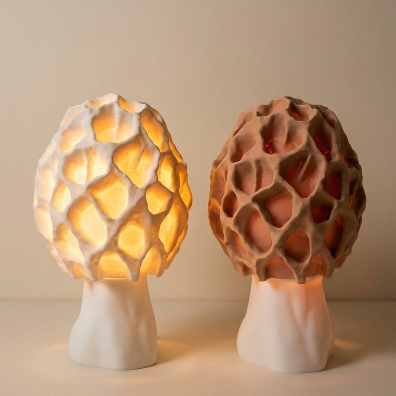 May include: Two mushroom-shaped lamps with textured, honeycomb-like caps. One lamp is white with a warm glow, the other is brown. Both have white stems and sit on a white surface. The lamps are decorative and provide ambient lighting.
