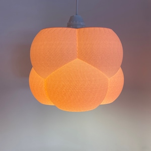 Op de afbeelding: Een witte hanglamp met een wolkvormige kap van een getextureerde stof. De kap wordt van binnenuit verlicht, waardoor een warm licht wordt gecreëerd.