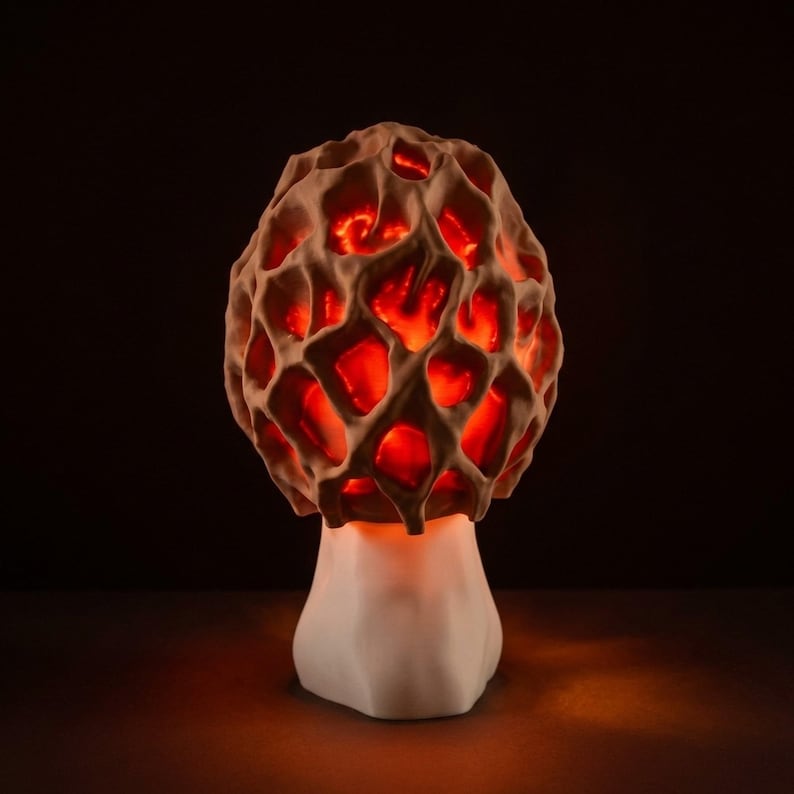 May include: A unique mushroom-shaped lamp with a textured, porous cap and a smooth, white base. The cap glows with a warm, red light, creating a cozy ambiance. The lamp is a decorative accent piece, perfect for adding a touch of nature-inspired design to any room.