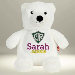 May include: A white plush polar bear with a black nose and eyes. The bear has a green and white crest with the letters CTR, and the name "Sarah Jackson" in purple and gold lettering.