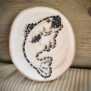 May include: A black string art design of a fish on a wooden slice. The fish is outlined with black string and has white beads for eyes.