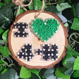 May include: A wooden round sign with the words "I 4-H" in black string wrapped around nails, and a green heart in the center.