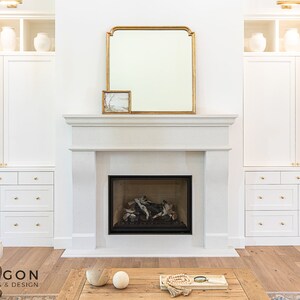 May include: A white fireplace with a black firebox and a gold framed mirror above it. The fireplace is flanked by white cabinets with gold hardware.