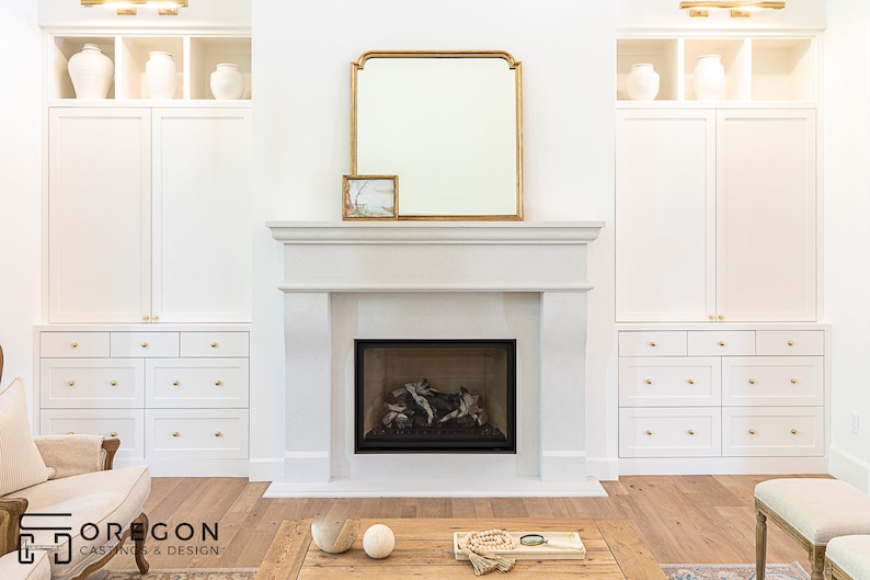 May include: A white fireplace with a black firebox and a gold framed mirror above it. The fireplace is flanked by white cabinets with gold hardware.