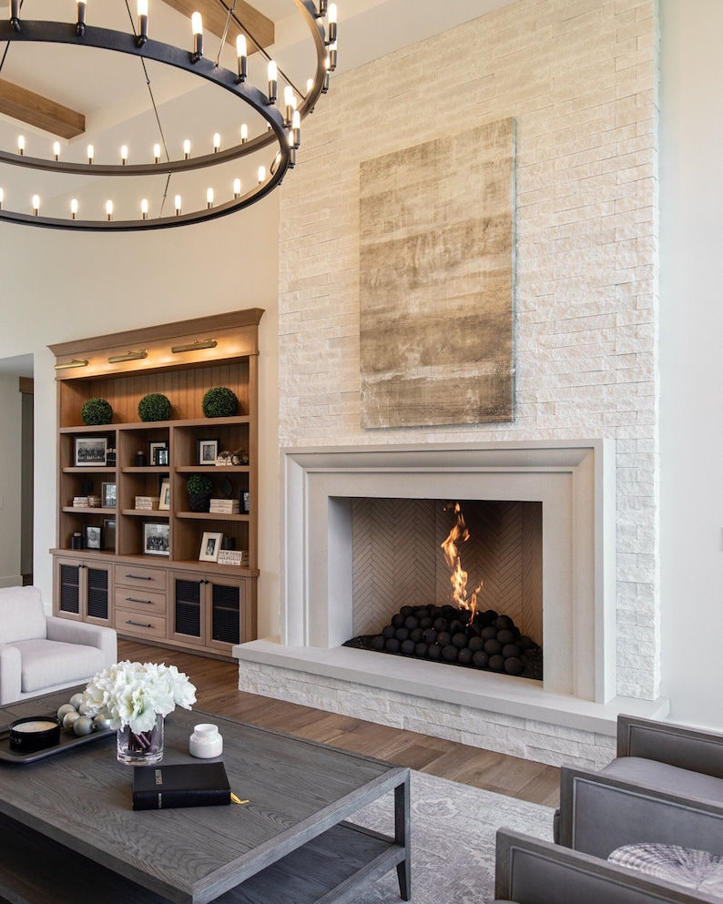 May include: A modern living room with a white brick fireplace, a large abstract painting above the fireplace, and a gray couch in the foreground.