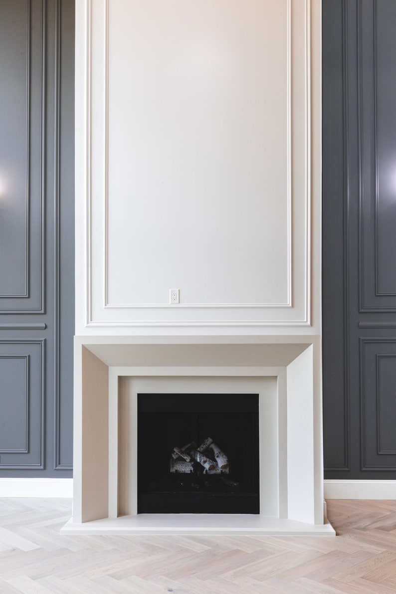 May include: A white fireplace with a black firebox and a white surround. The fireplace is set against a dark gray wall.