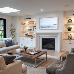 May include: A living room with a large sectional sofa, two armchairs, a coffee table, and a fireplace. The room has a skylight, large windows, and built-in shelves with decorative items.