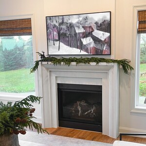 May include: A white fireplace with a black fireplace insert and a framed painting of a snowy village scene above it. A green garland with a deer figurine is draped across the mantel.