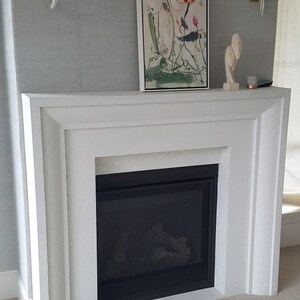 May include: White fireplace surround with a black gas fireplace insert. The fireplace is decorated with a framed painting of flowers and a small sculpture.