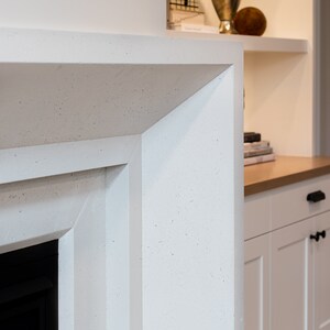 May include: Close-up of a white fireplace surround with a textured finish. The surround has a sharp, angled edge and is made of a material that resembles concrete.