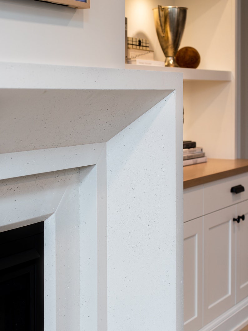 May include: Close-up of a white fireplace surround with a textured finish. The surround has a sharp, angled edge and is made of a material that resembles concrete.