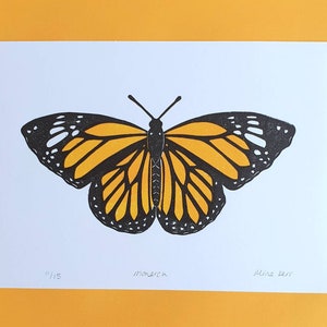 Op de afbeelding: Een zwart-oranje monarchvlinderprint op wit papier. De print is genummerd "1/15" en gesigneerd "Alina Kerr".