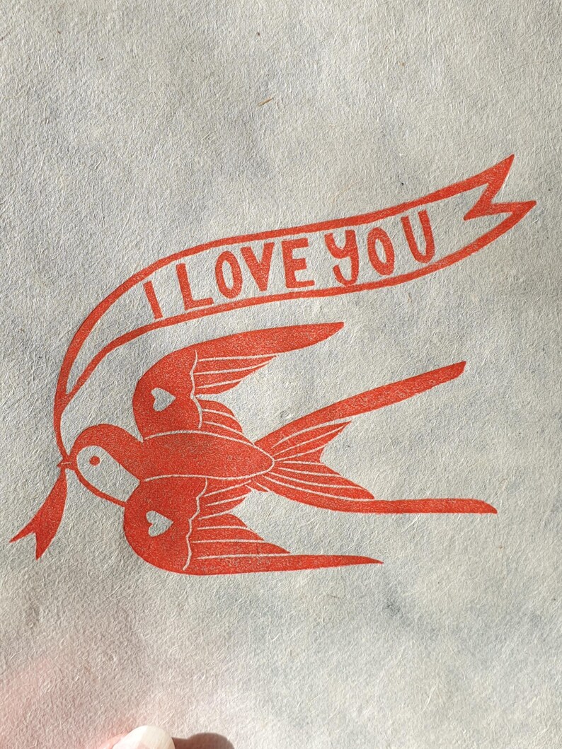 Op de afbeelding: Rode illustratie van twee vogels met harten op hun vleugels, die vliegen met een banner waarop "I LOVE YOU" staat.