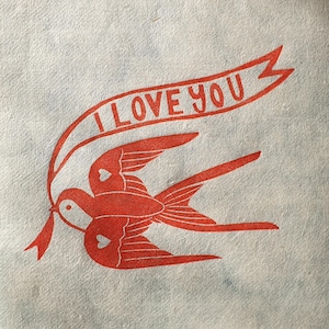 Op de afbeelding: Rode en witte illustratie van een vogel die een banner draagt met de tekst "I LOVE YOU".