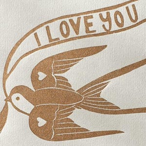 Op de afbeelding: Twee bruine vogels met harten op hun borst vliegen samen met een banner waarop "I LOVE YOU" staat.