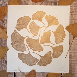 May include: A gold print of a ginkgo leaf design on a white background. The print is titled "Ginkgo Golden" and signed "Mina Kerr".
