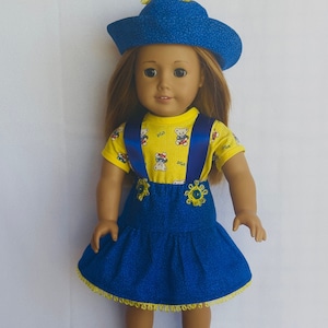 May include: A doll wearing a blue and yellow outfit. The doll is wearing a blue hat with yellow flowers, a yellow shirt with blue suspenders, a blue skirt with yellow trim, and white shoes.