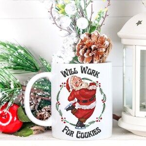 May include: White ceramic mug with a red and white illustration of Santa Claus ice skating. The mug has black text that reads "Will Work For Cookies".