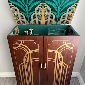 May include: A wooden cabinet with gold accents and a green patterned top. The cabinet has two doors with gold handles and a green interior. The cabinet is on a wooden floor.