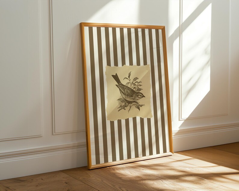 Op de afbeelding: Een ingelijst kunstwerk met een vintage vogelillustratie. Het kunstwerk heeft een gestreepte achtergrond van bruine en cr&egrave;mekleurige verticale lijnen. De vogelillustratie staat op een gescheurd, verouderd papier. De lijst is lichtbruin.