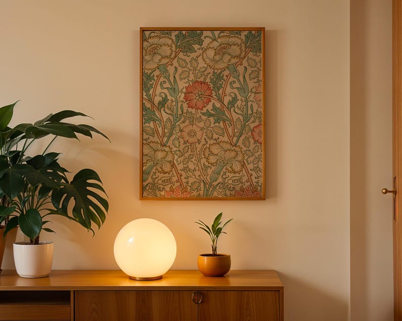 May include: A white glass globe lamp with a wooden base sits on a wooden table next to a potted plant. A framed floral print hangs on the wall behind the lamp.