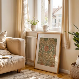 May include: A beige sofa with a book on it, a framed print with a floral design, a potted plant, and a window with sunlight streaming in.