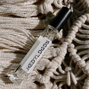 May include: A clear glass bottle with a black cap and a white label that says "HEDY" in a handwritten font. The bottle is sitting on a white crocheted surface.