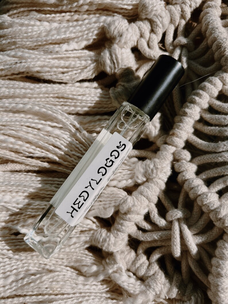 May include: A clear glass bottle with a black cap and a white label that says "HEDY" in a handwritten font. The bottle is sitting on a white crocheted surface.