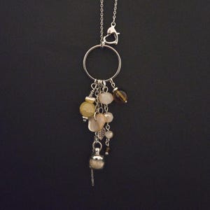 Peut inclure: Collier argenté avec un grand pendentif circulaire orné d'un groupe de perles jaunes, marron et blanches. Un petit charme en forme de feuille et une perle décorative sont également inclus. Le collier a un fermoir en forme de cœur.
