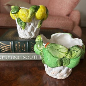 May include: Two ceramic planters featuring a lattice-style base. One planter is decorated with yellow lemons and green leaves around the rim, while the other features green pears and green leaves around the rim. Both have a white interior finish.