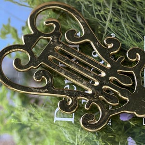 May include: An ornate, gold-coloured metal decorative key-shaped object with scrollwork and a central slotted design. The object rests on a book with the text "an Howard" and green foliage.