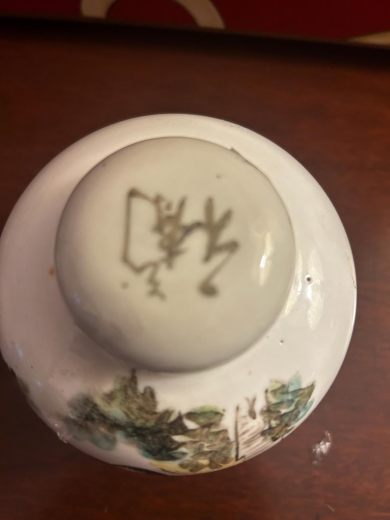 Pu&ograve; includere: Un coperchio in ceramica bianca con un pomello rotondo con un carattere asiatico. Il coperchio presenta un disegno paesaggistico dipinto in verde, blu e marrone. Il coperchio &egrave; probabilmente per un barattolo o un contenitore.