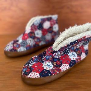 May include: A pair of red, blue, and white patchwork slippers with a white fleece lining. The slippers have a brown sole.